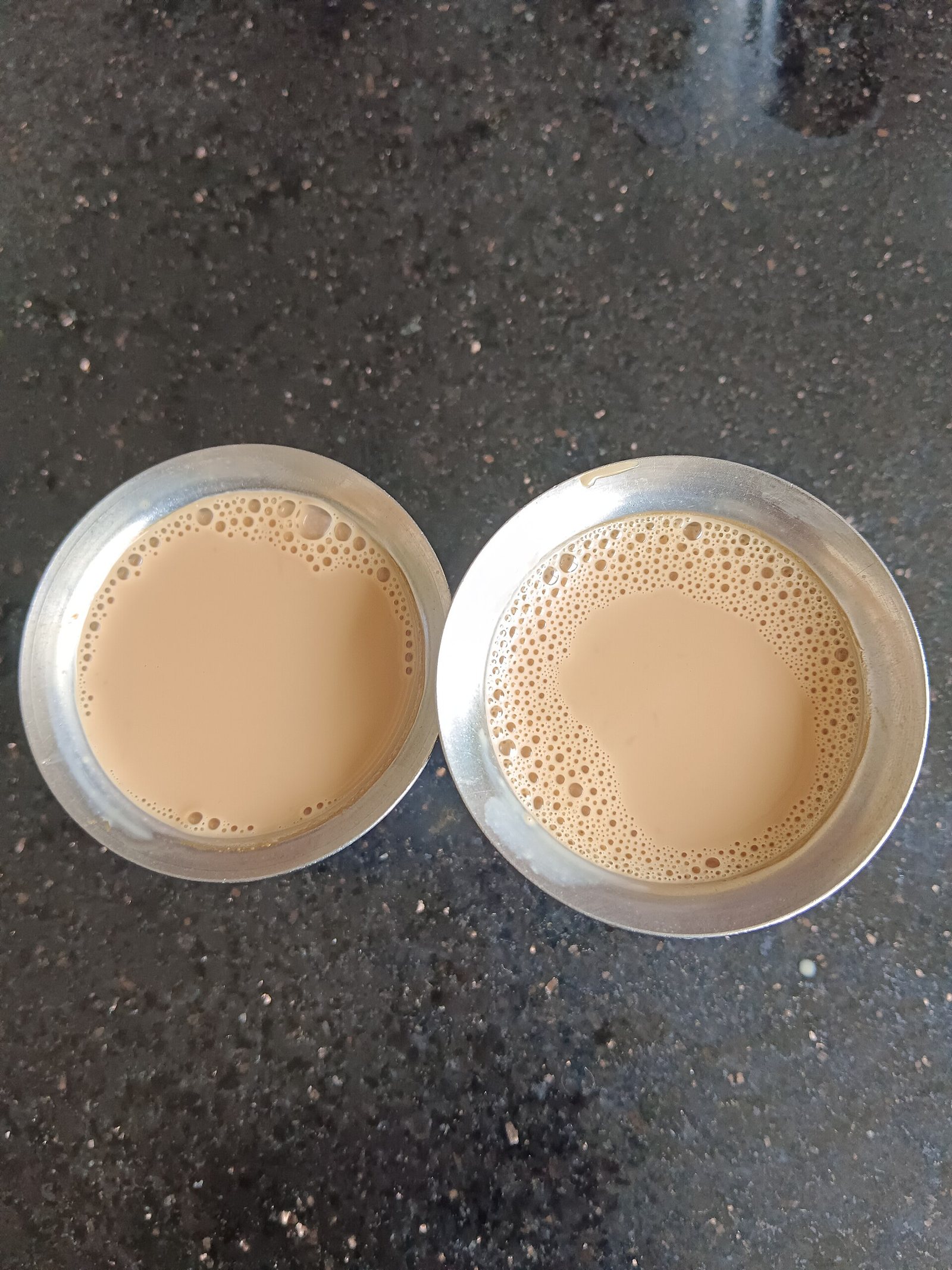 Two cups of chai on a dark counter, seen from above