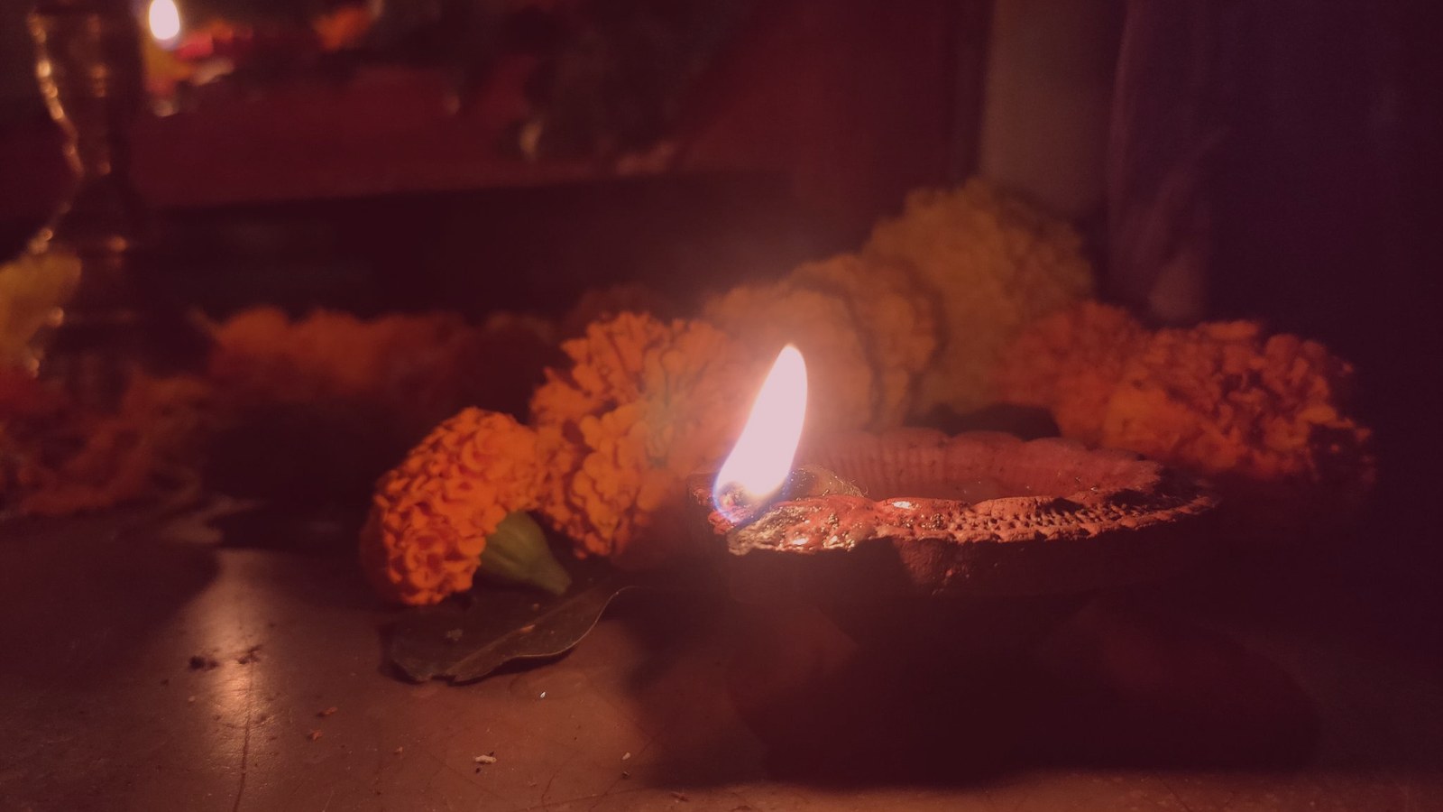 A lit oil lamp beside marigold flowers in warm rose light